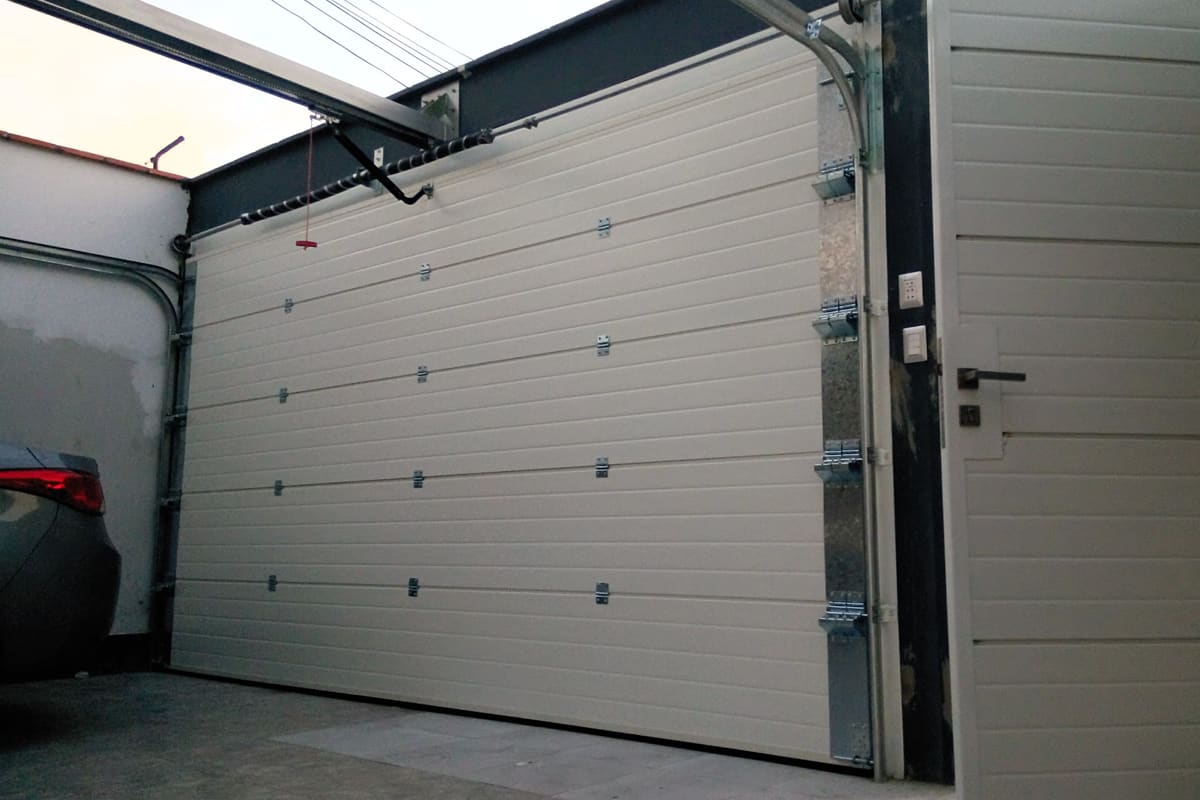 Puerta seccional con panel sandwich importado instalada en fachada